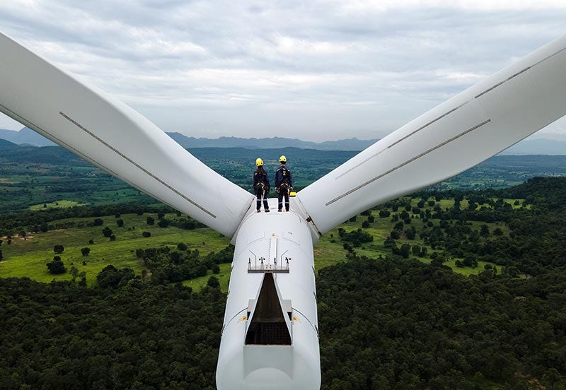 Two electrical engineers wearing PPE working on top of wind turbine farm