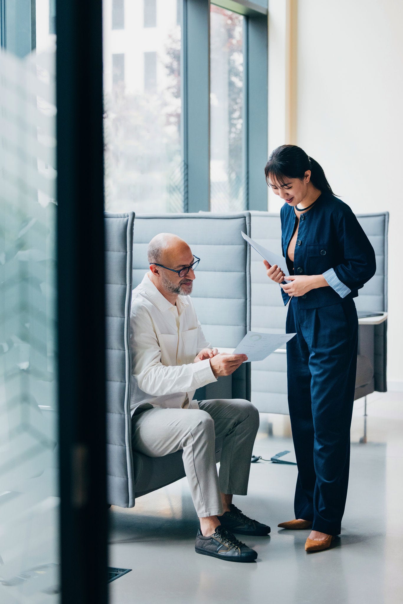 Two colleagues engage in a work discussion, sharing documents and ideas in a contemporary workplace environment with an open, collaborative design.