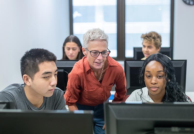 High school teacher helping students with assignment in computer lab