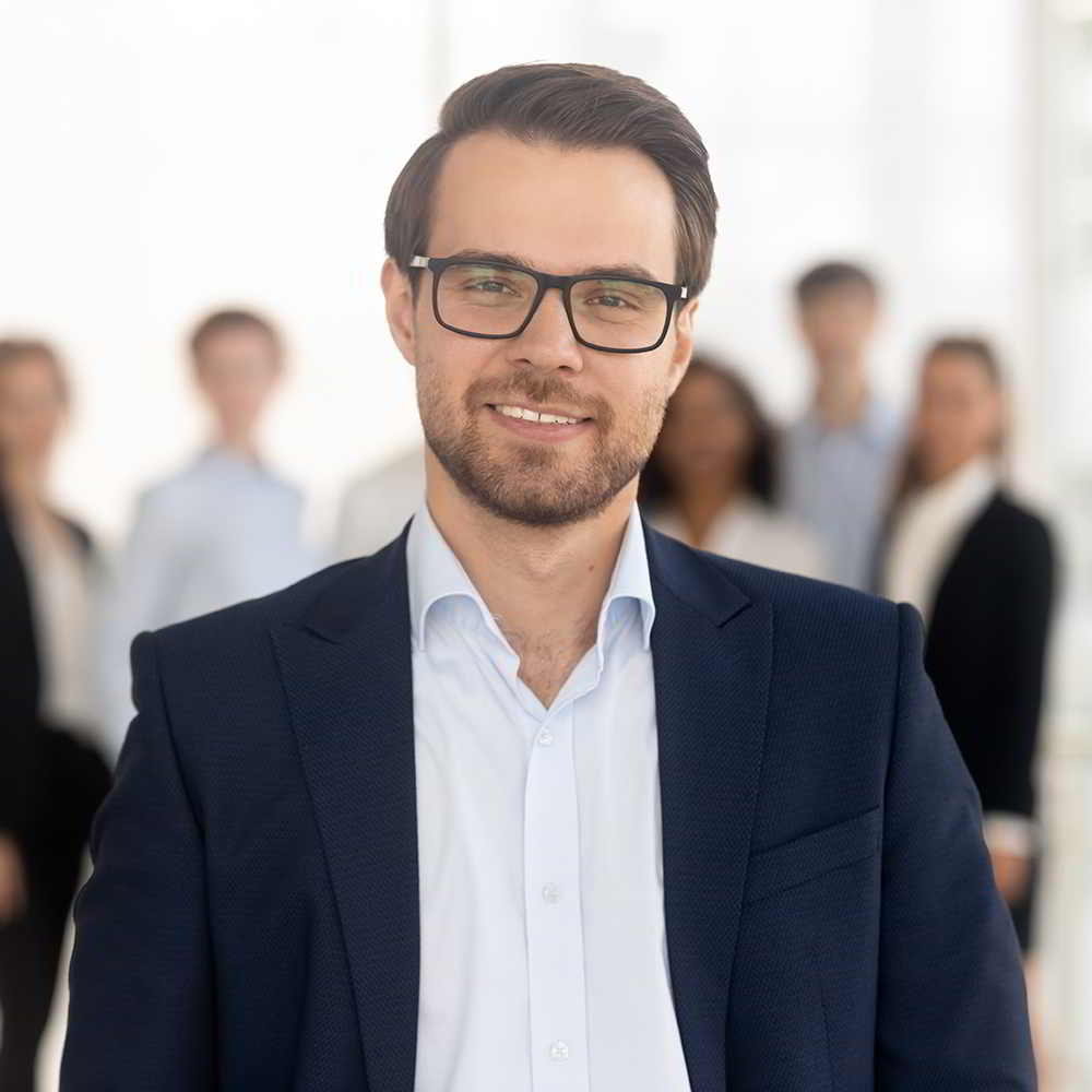 Man in office looking into camera with team behind him