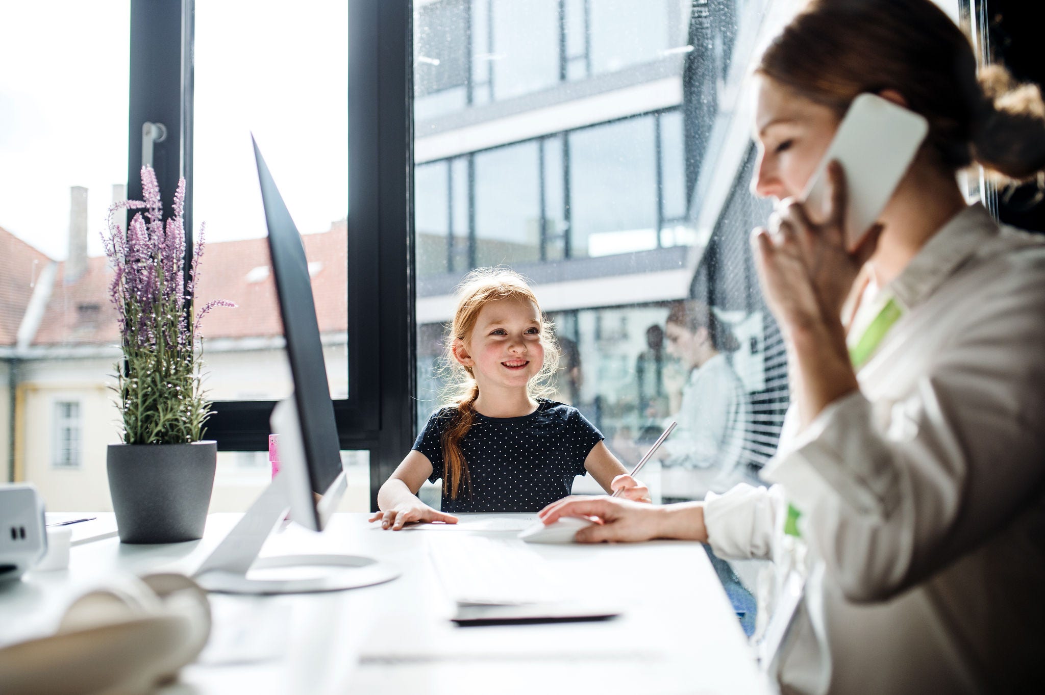 A businesswoman with a small daughter sitting in an office, working.