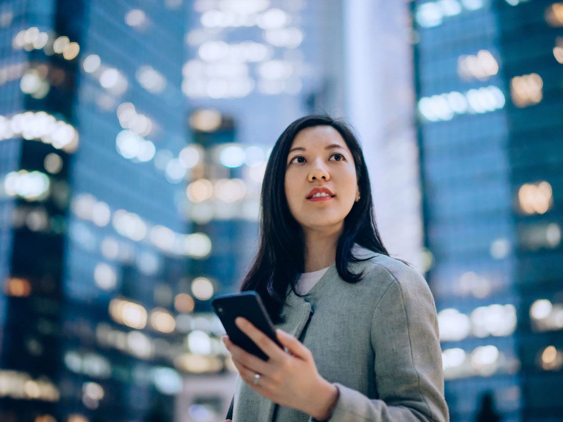 Business woman holding phone in front of skyscrapers