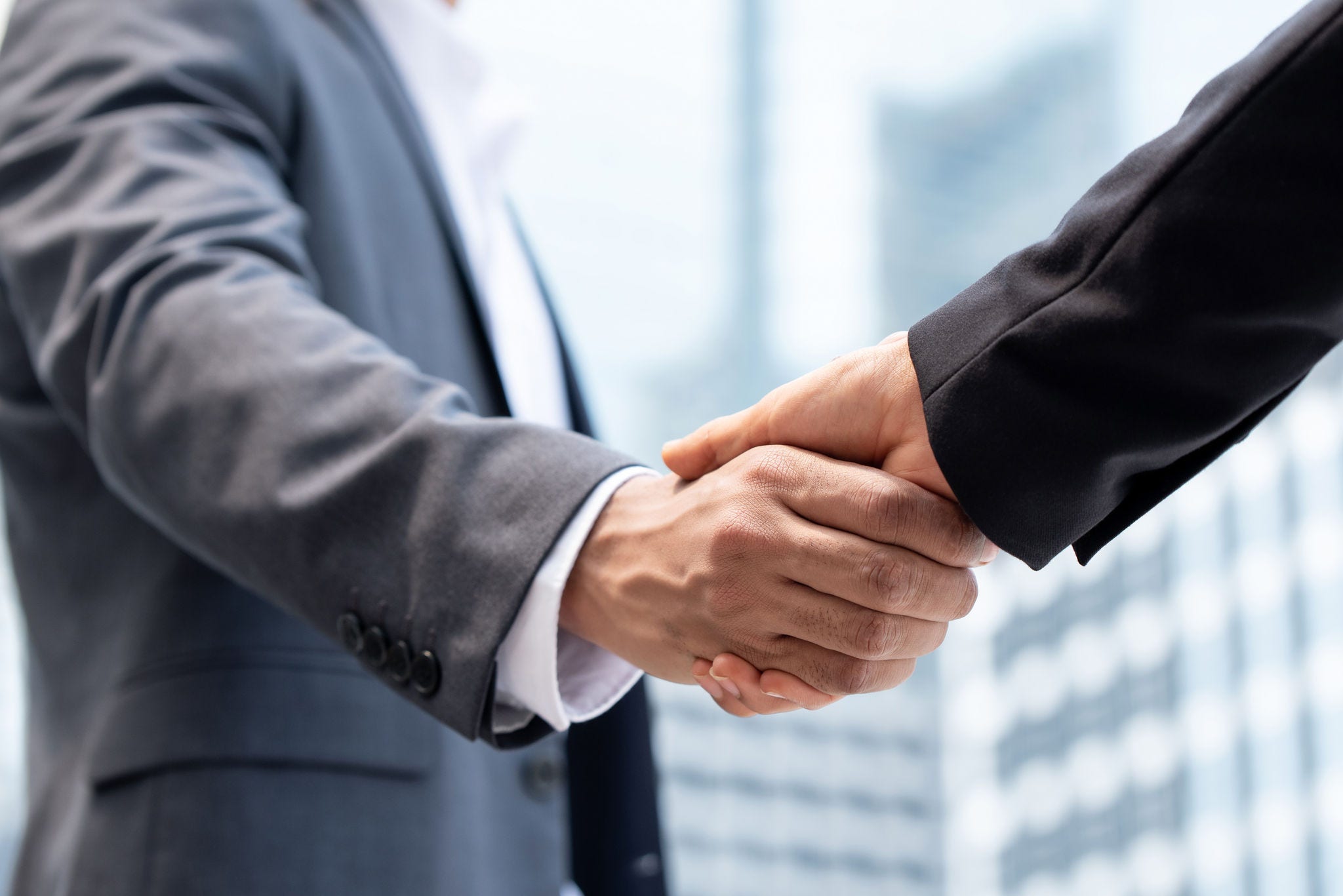 Businessmen making handshake outdoors in city office building background for merger and acquisition concept