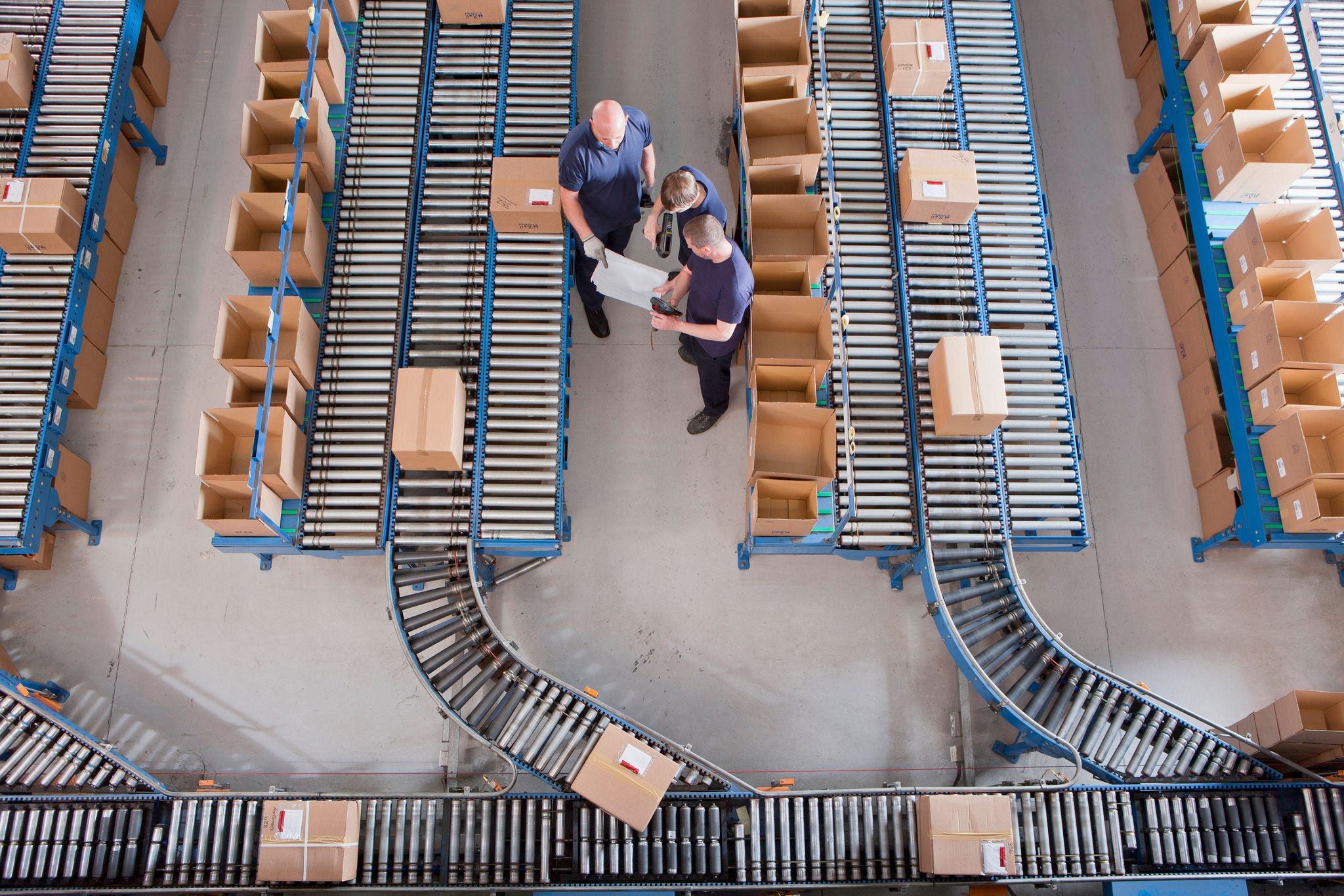 Workers meeting among boxes on conveyor belts in distribution warehouse