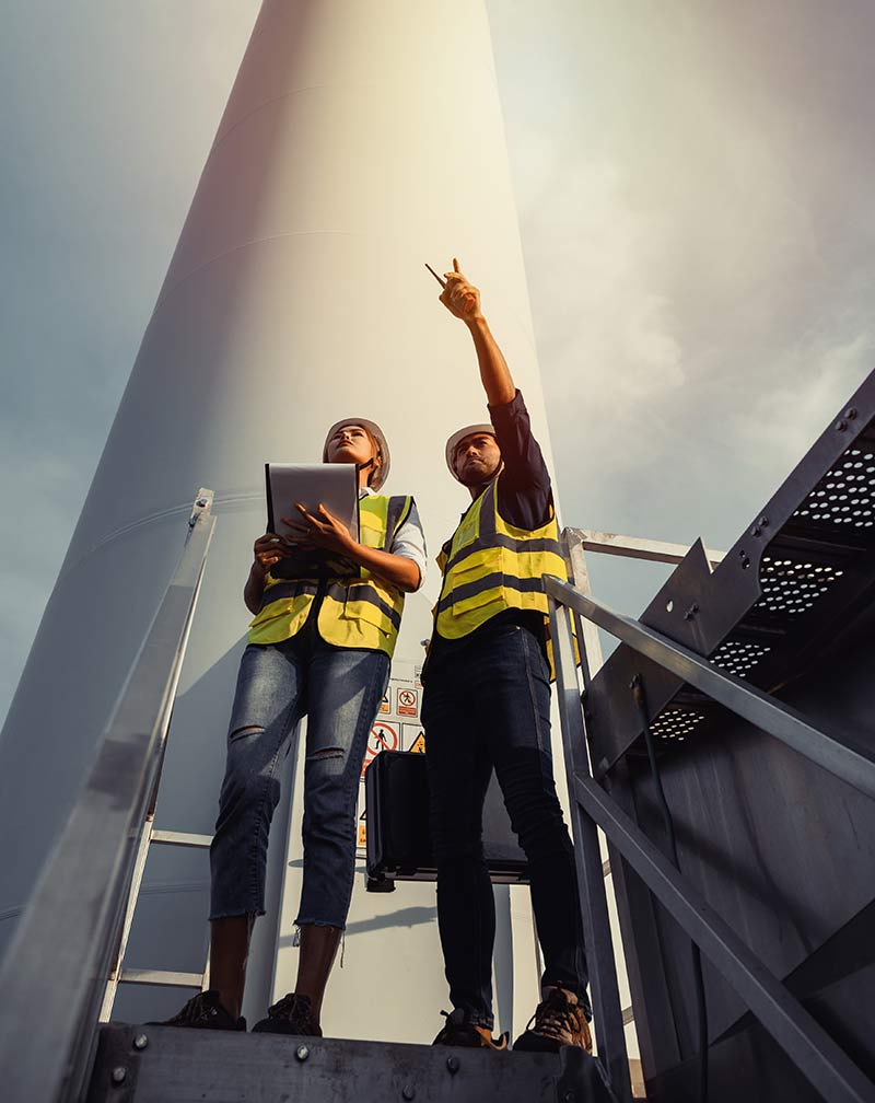 Two construction workers standing next to a windmill