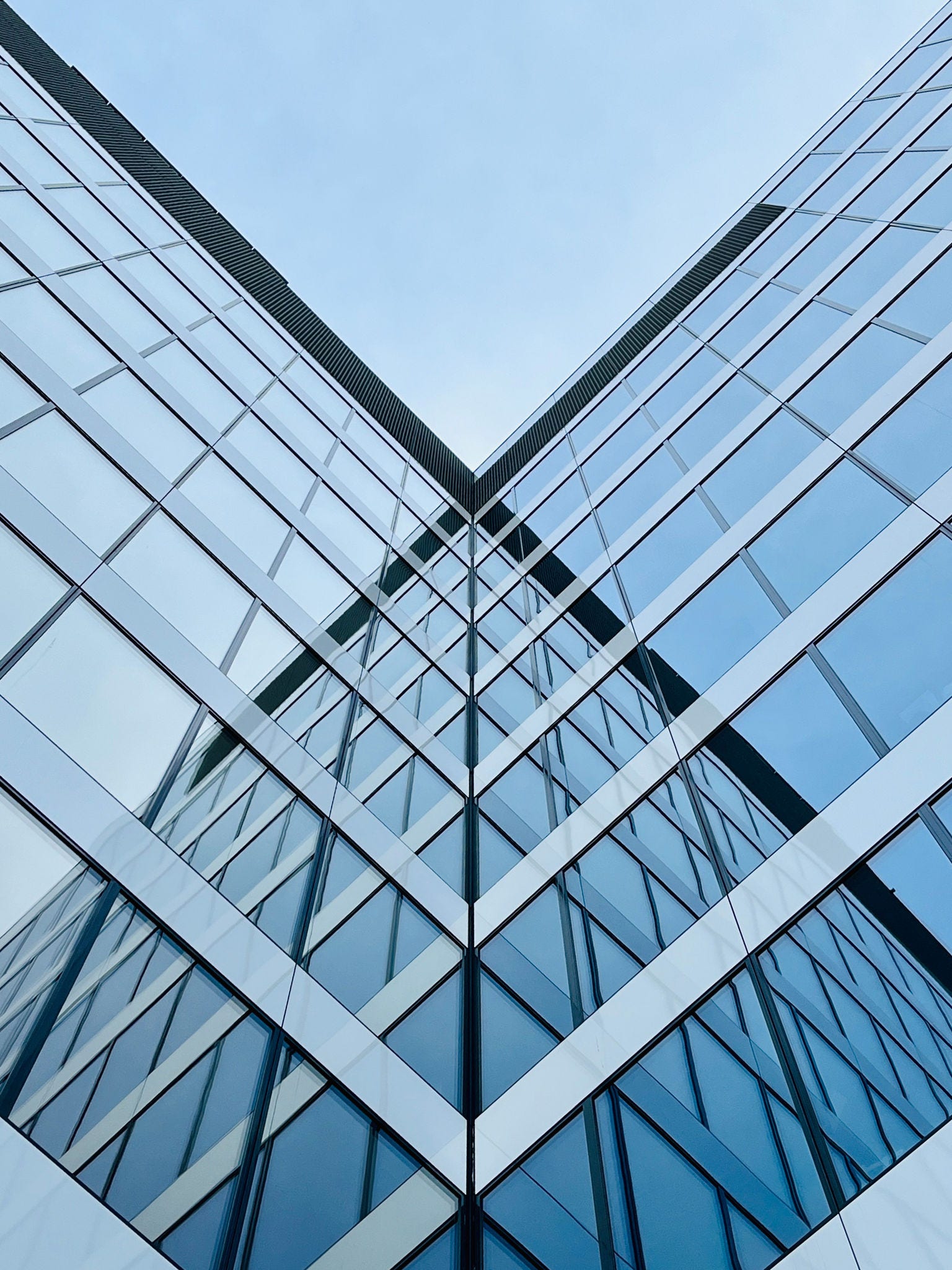 Low angle view of a modern office skyscraper, featuring sleek, reflective windows. The urban architecture is captured in an abstract, geometric, and minimalist style, highlighting the clean lines and contemporary design of the building.