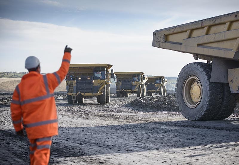 Mine worker waving at dumpers driving on track at surface coal mine